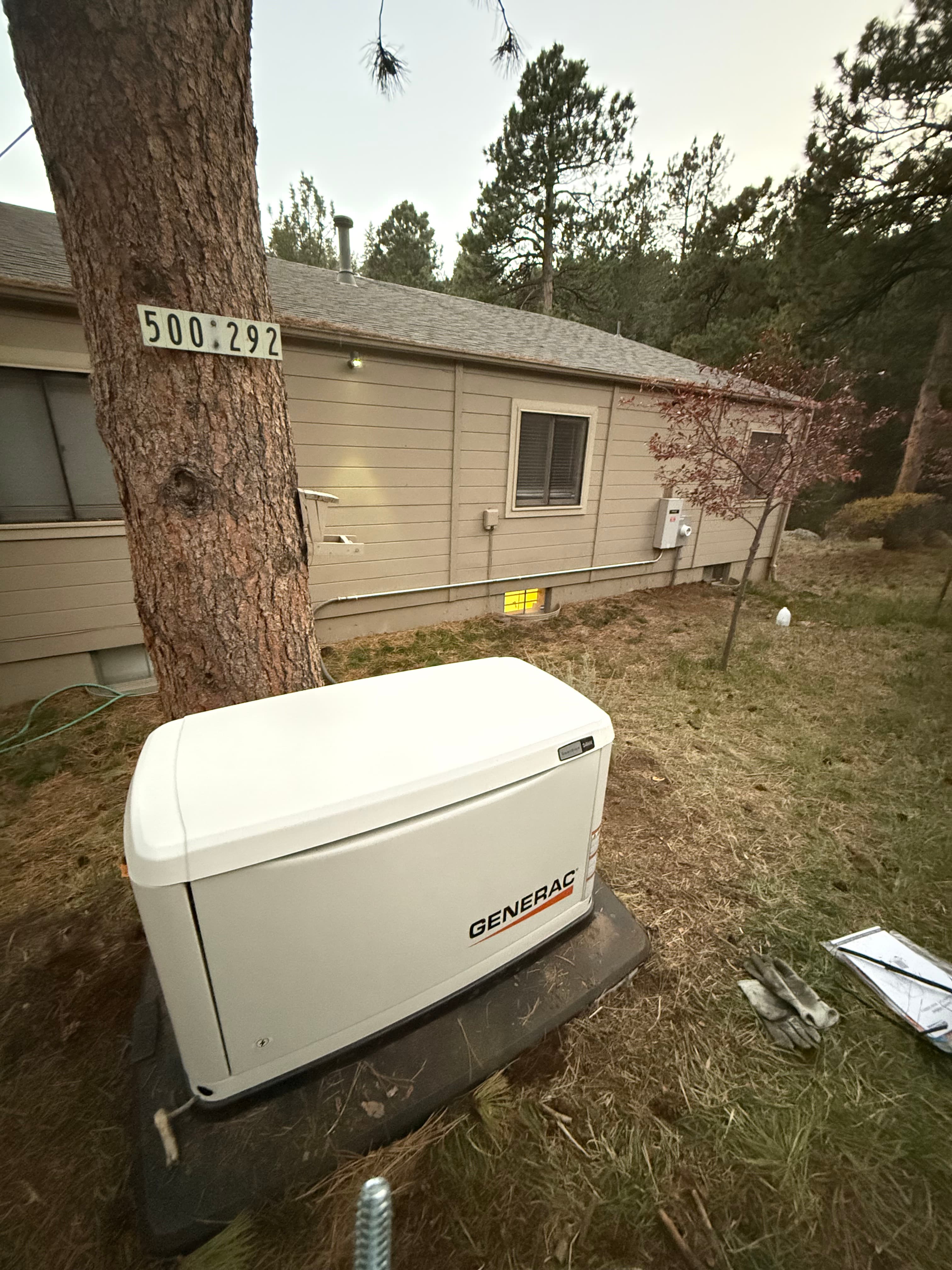 White Generac standby generator on a pad in a grassy yard beside a tan house.